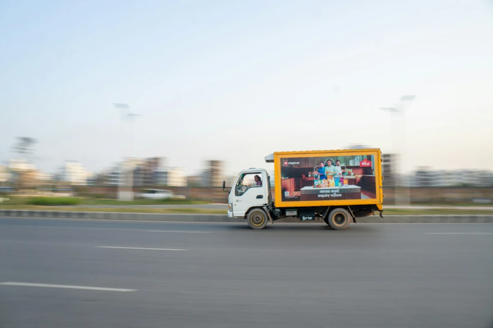 A white truck drives on a road with an advertisement.